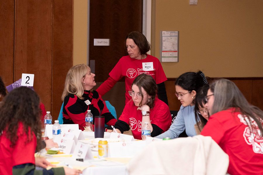 Professor Dianna Hess stands by a table of participants and talks with the Vice Chancellor of Student Affairs