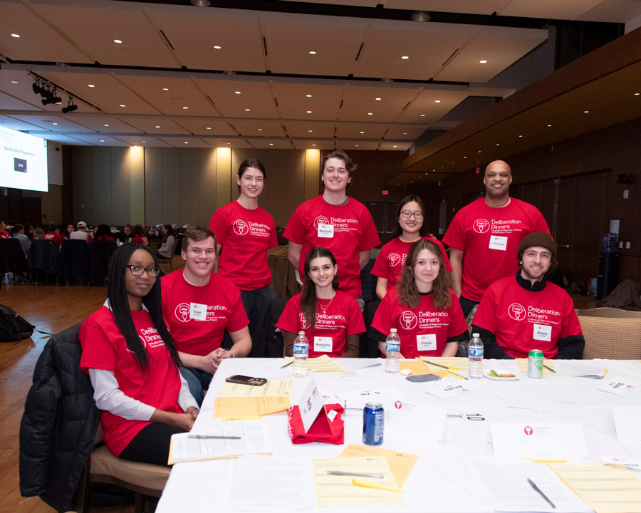 A group of 9 participants at a table and smiling for the camera
