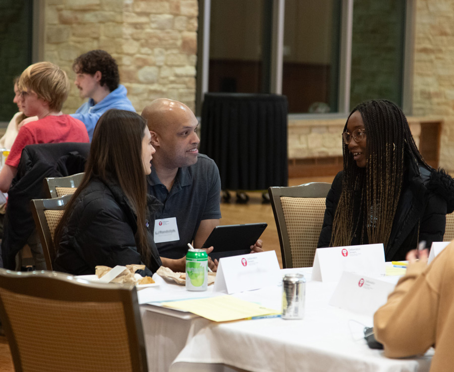 3 people having a conversation. One person is actively listening and smiling.
